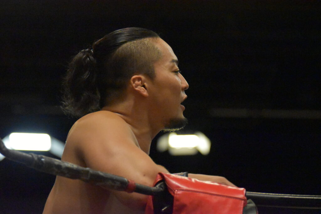 A side profile of a young man with prominent cheekbones and a black ponytail, seriously watching a match unfold.